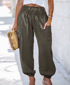 Woman wearing Serenity High-Waist Comfort Pants in beige and olive colors, paired with a white crop top and heels, carrying a decorative clutch.