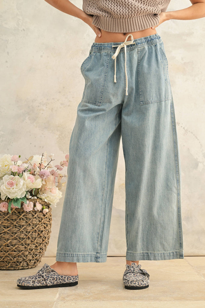 Woman wearing light wash wide-leg denim pants with elastic drawstring waist and front patch pockets.