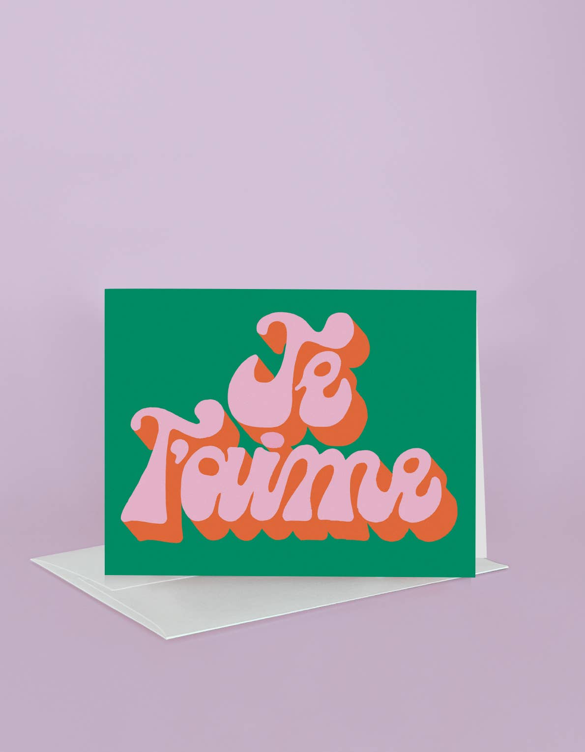 Card with 'Je T'aime' text on a green background with a pink border, on a light purple background.