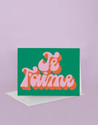 Card with 'Je T'aime' text on a green background with a pink border, on a light purple background.