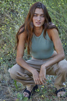 Woman wearing a fitted waffle-texture cropped tank top in green and white, styled with casual denim and neutral pants.