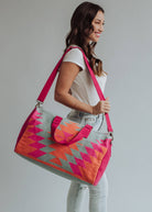 Vibrant weekender bag with orange and hot pink geometric design, held by woman in light wash jeans and white tank top