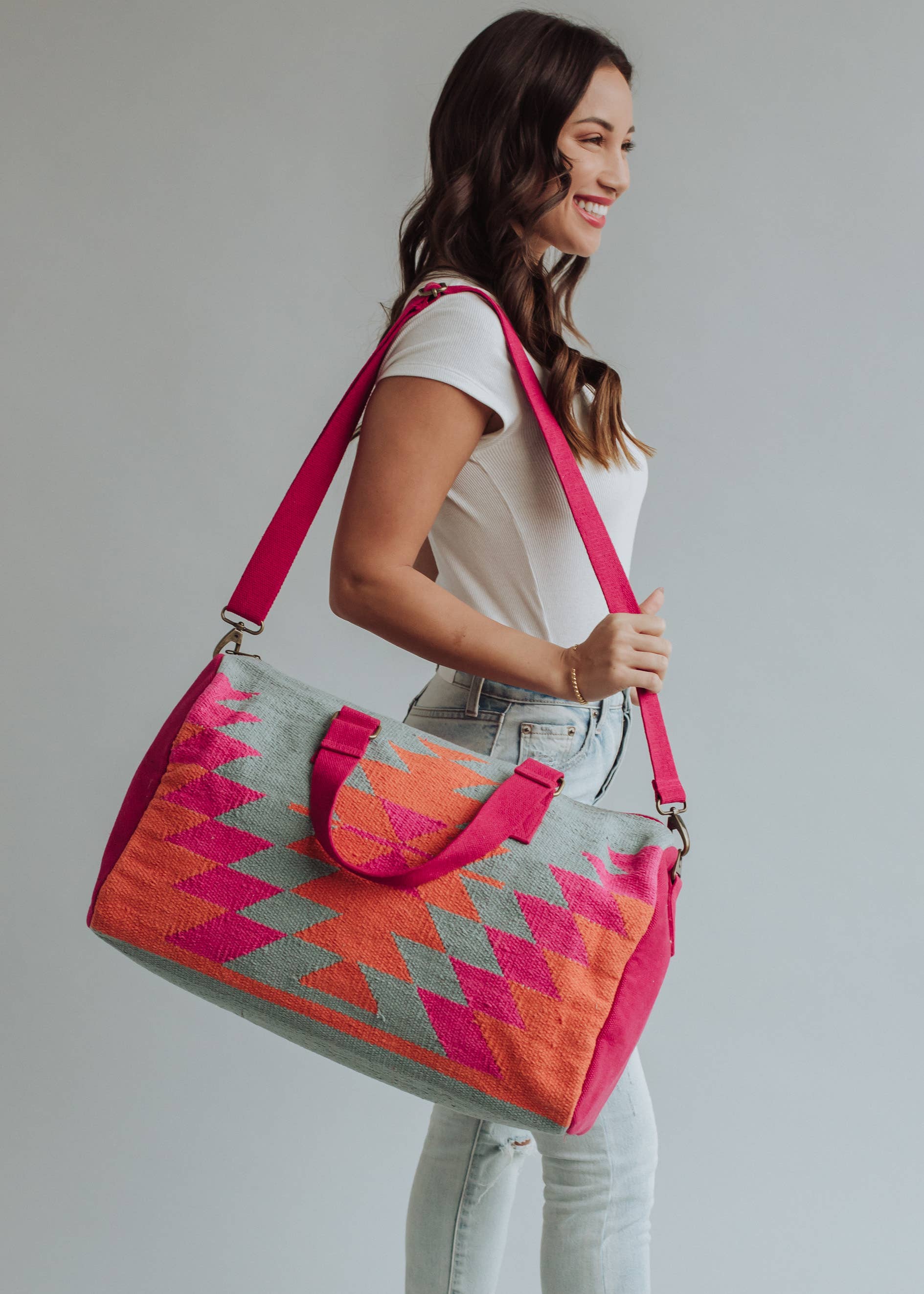 Vibrant weekender bag with orange and hot pink geometric design, held by woman in light wash jeans and white tank top