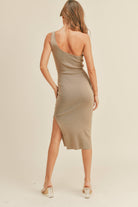 Model wearing a beige one-shoulder ribbed dress with a side slit, posing confidently.