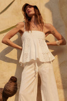 Woman wearing white embroidered cami top with eyelet detail and flared hem in natural sunlight.