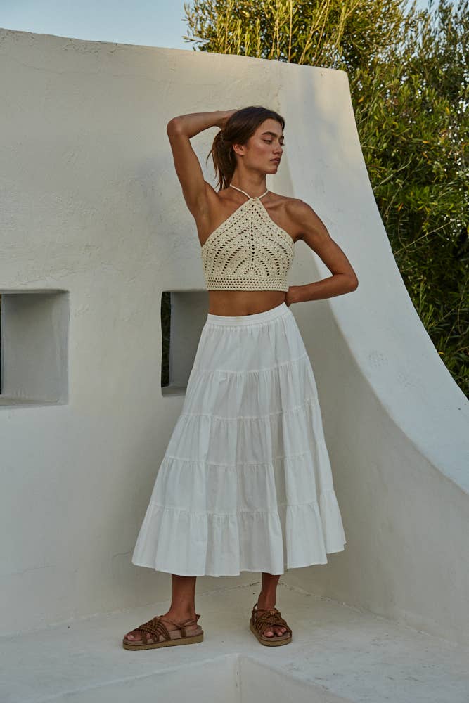 Model wearing a crochet halter crop top in black and cream, styled with jeans and a skirt, showing detailed open-stitch design.