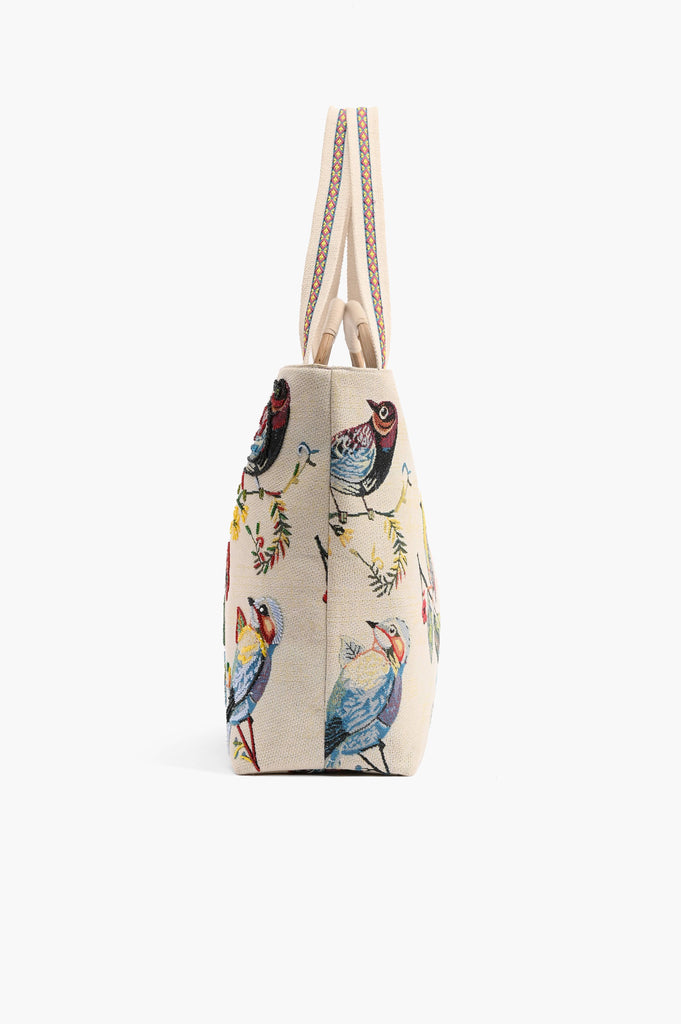Beige embroidered tote bag with colorful birds, butterflies, and leaves, featuring round woven handles and shoulder strap.