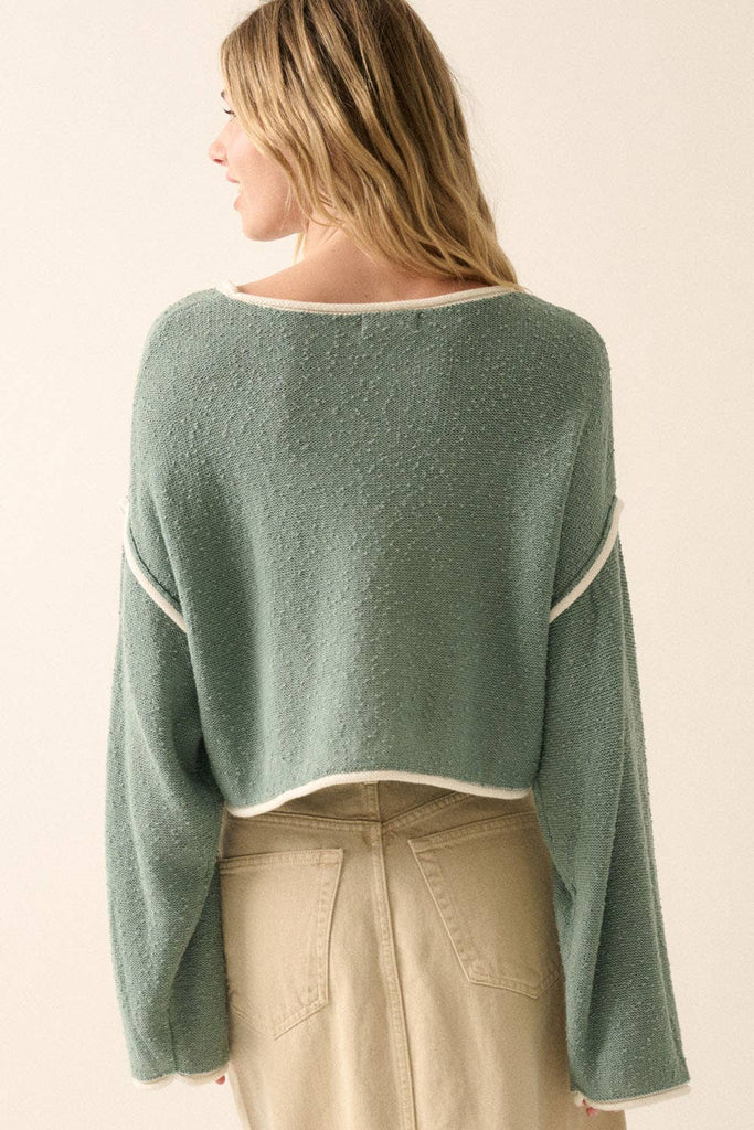 Woman wearing a sage green off-shoulder cropped sweater with white trim details and long sleeves.