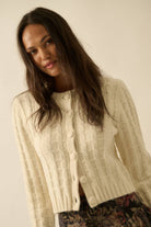 Woman wearing a cream textured knit cardigan with covered buttons, styled with a floral skirt.