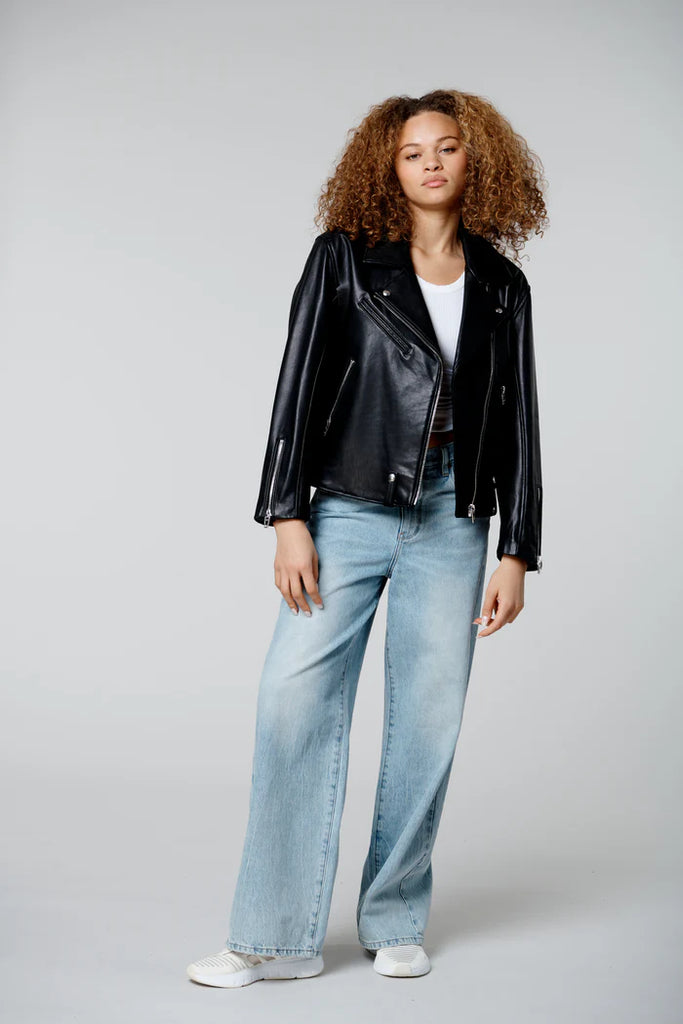 Person wearing a black leather jacket and light blue jeans on a gray background