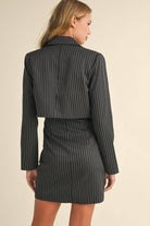 Woman wearing a black pinstriped strapless midi dress with a matching cropped blazer jacket.