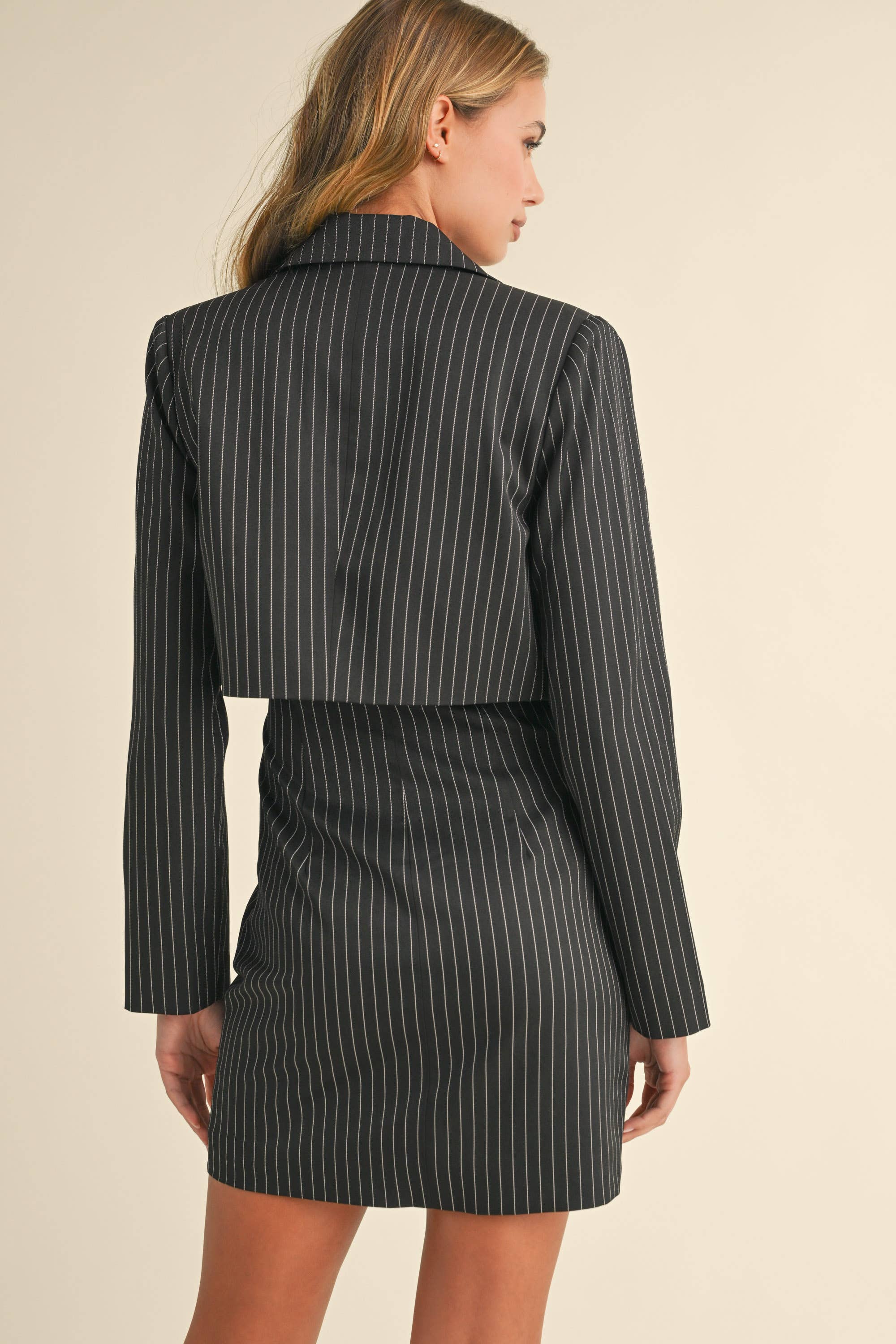 Woman wearing a black pinstriped strapless midi dress with a matching cropped blazer jacket.