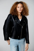 Person wearing a black leather jacket and light blue jeans on a plain background