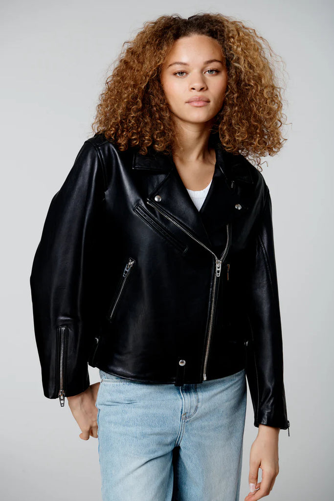 Person wearing a black leather jacket and light blue jeans on a plain background