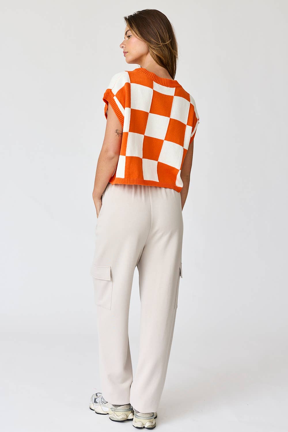 Woman wearing an orange and white loose-fit checker knit top with beige pants.