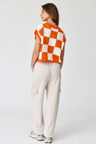 Woman wearing an orange and white loose-fit checker knit top with beige pants.