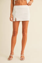 White two-piece set with square-neck top, open back detail, and matching mini skirt with slit, worn by model