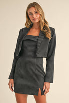 Woman wearing a black pinstriped strapless midi dress with a matching cropped blazer jacket.