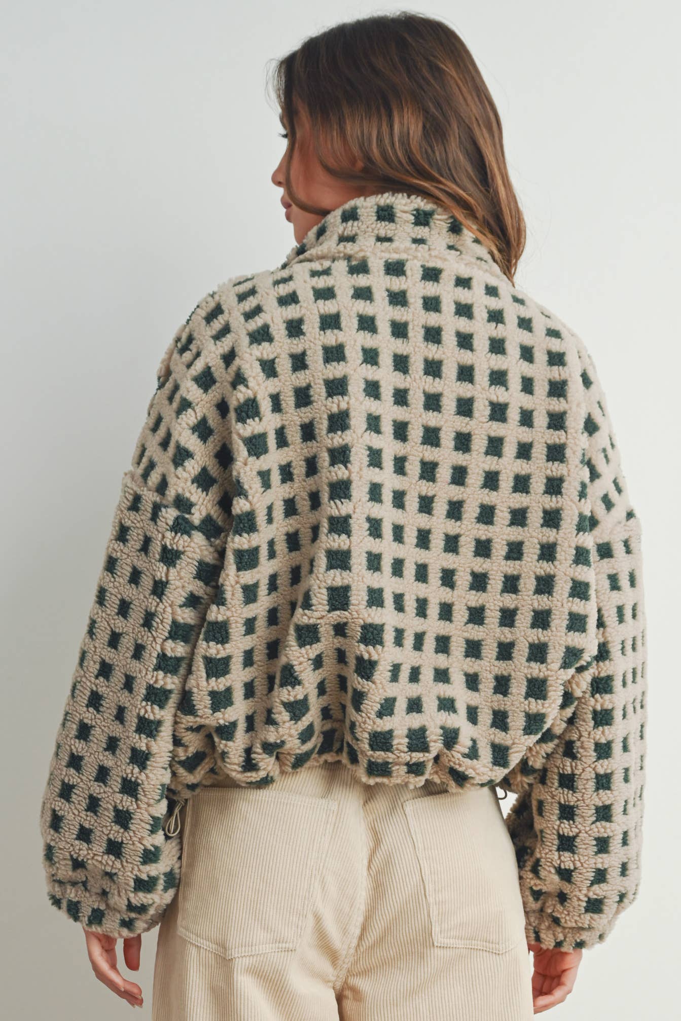 Woman wearing a beige and green checkered fleece jacket with a zip closure, paired with a white crop top and beige corduroy pants.