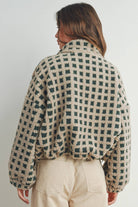 Woman wearing a beige and green checkered fleece jacket with a zip closure, paired with a white crop top and beige corduroy pants.