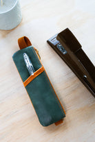 Green leather pen case with a pen inside on a wooden surface