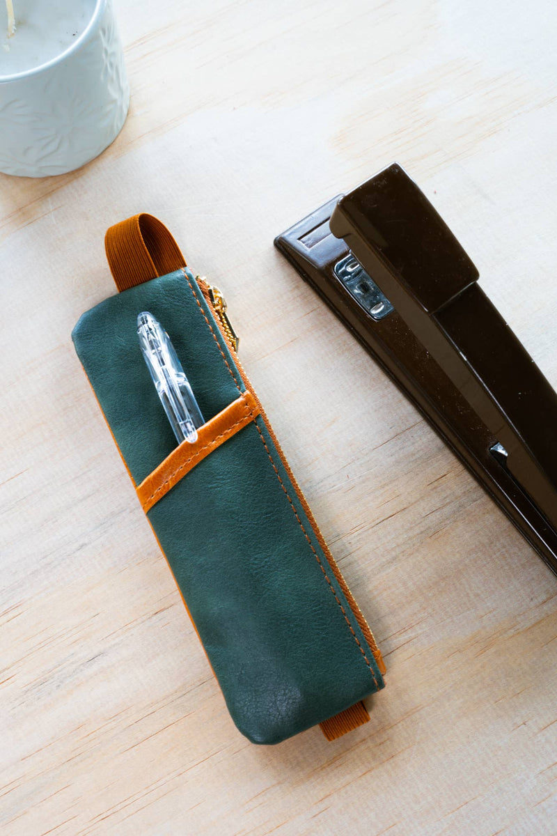 Green leather pen case with a pen inside on a wooden surface