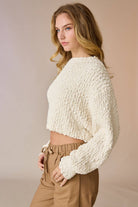 Woman wearing a cream popcorn knit cropped sweater with tan drawstring pants, hands in pockets.