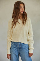 Woman wearing a cream chunky knit pullover sweater with relaxed fit, styled casually with light-wash jeans.