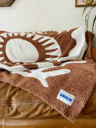Soft brown plush throw blanket with a sun and palm tree design, perfect for adding warmth and a stylish accent to any space.