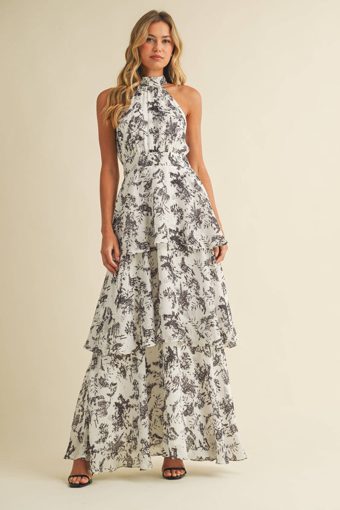 Woman wearing a halter neck tiered maxi dress with black floral print and ruffle layers