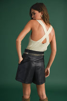 Model wearing a sleeveless ribbed knit top with deep V-neck and cross-back strap detail.