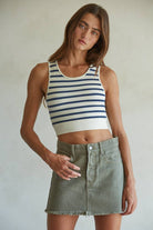 Model wearing a ribbed cropped racerback tank with navy and cream horizontal stripes, styled with an olive mini skirt.