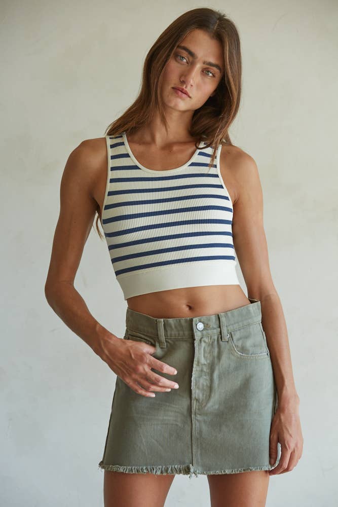 Model wearing a ribbed cropped racerback tank with navy and cream horizontal stripes, styled with an olive mini skirt.