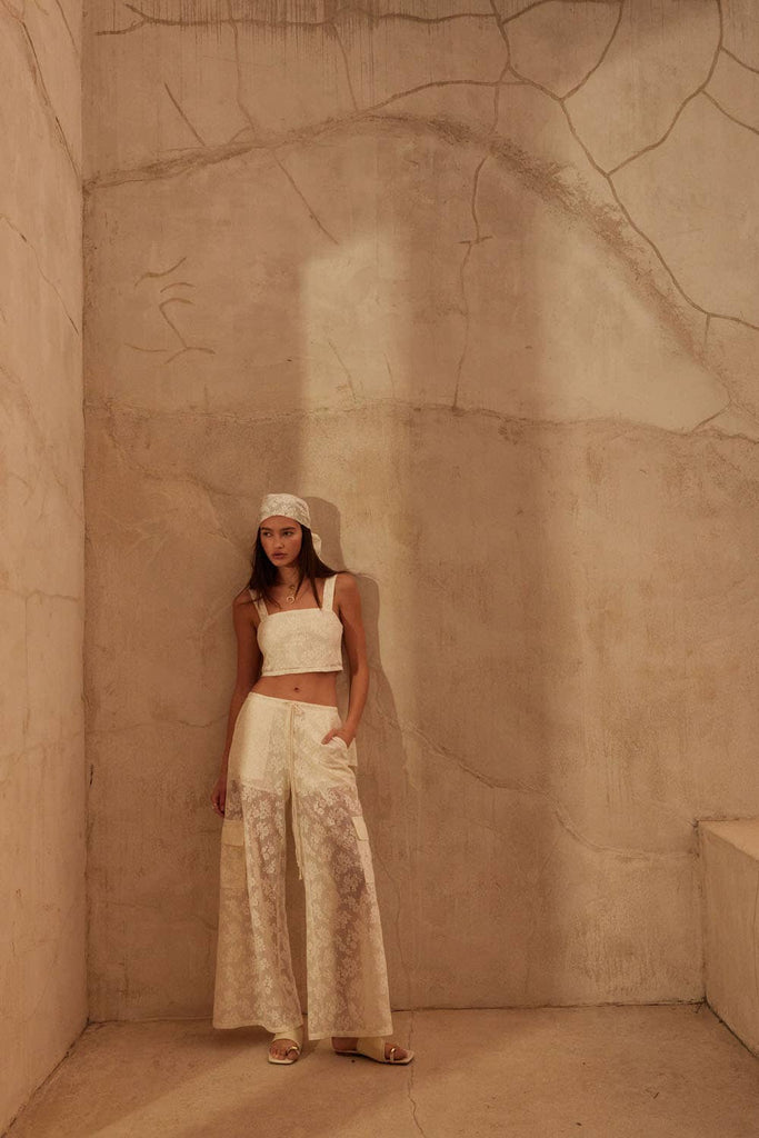 Model wearing ivory lace two-piece set with cropped top and drawstring wide-leg pants.
