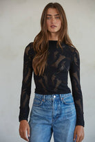 Model wearing the Celestine Lace Top in cream and black lace with long sleeves and floral mesh pattern