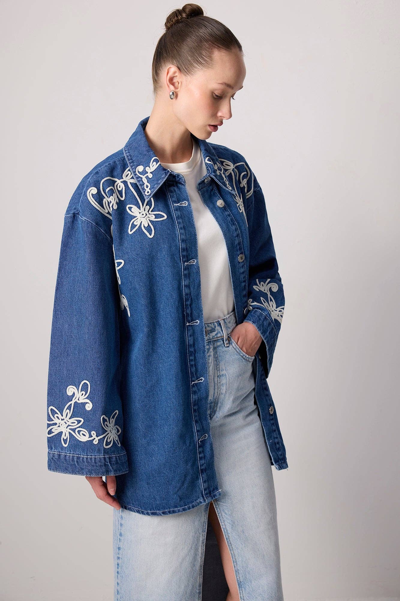 Model wearing a belted denim jacket with white floral embroidery and wide sleeves