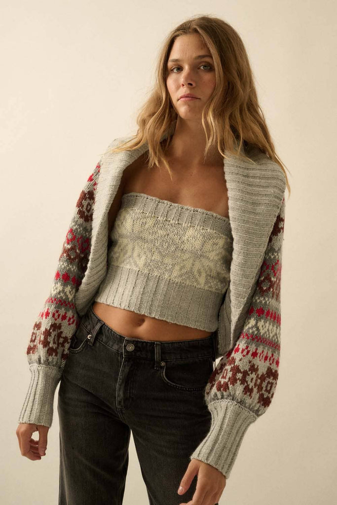 Woman wearing a patterned cardigan over a crop top and jeans on a plain background
