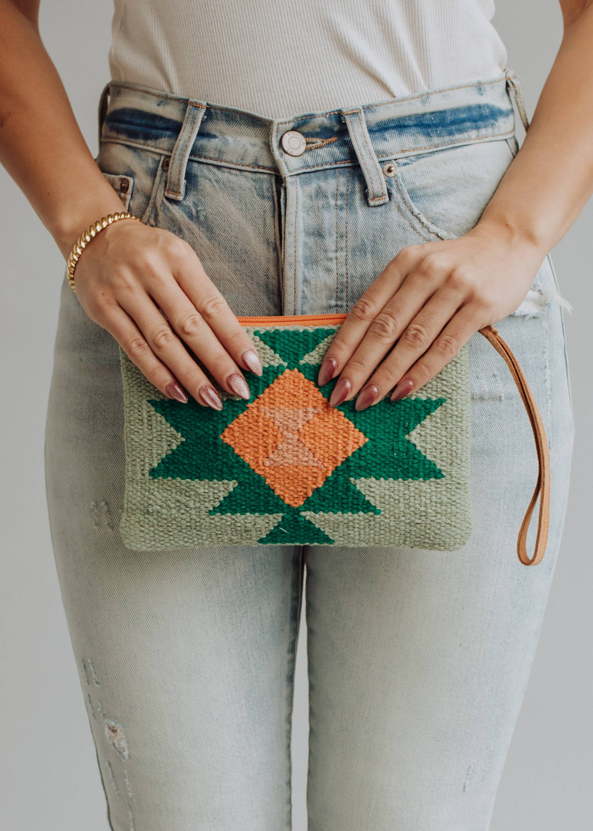 Sage green woven wristlet with orange and emerald geometric pattern, worn with light denim
