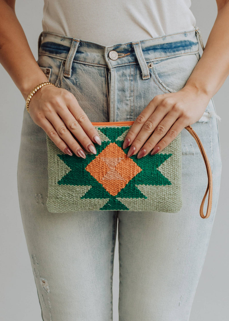 Sage green woven wristlet with orange and emerald geometric pattern, worn with light denim
