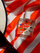 Poom Poom Eau de Parfum bottle with playful illustrations, displayed on an orange and white striped fabric background.