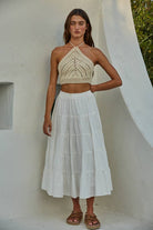 Model wearing a crochet halter crop top in black and cream, styled with jeans and a skirt, showing detailed open-stitch design.