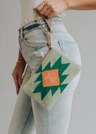 Sage green woven wristlet with orange and emerald geometric pattern, worn with light denim
