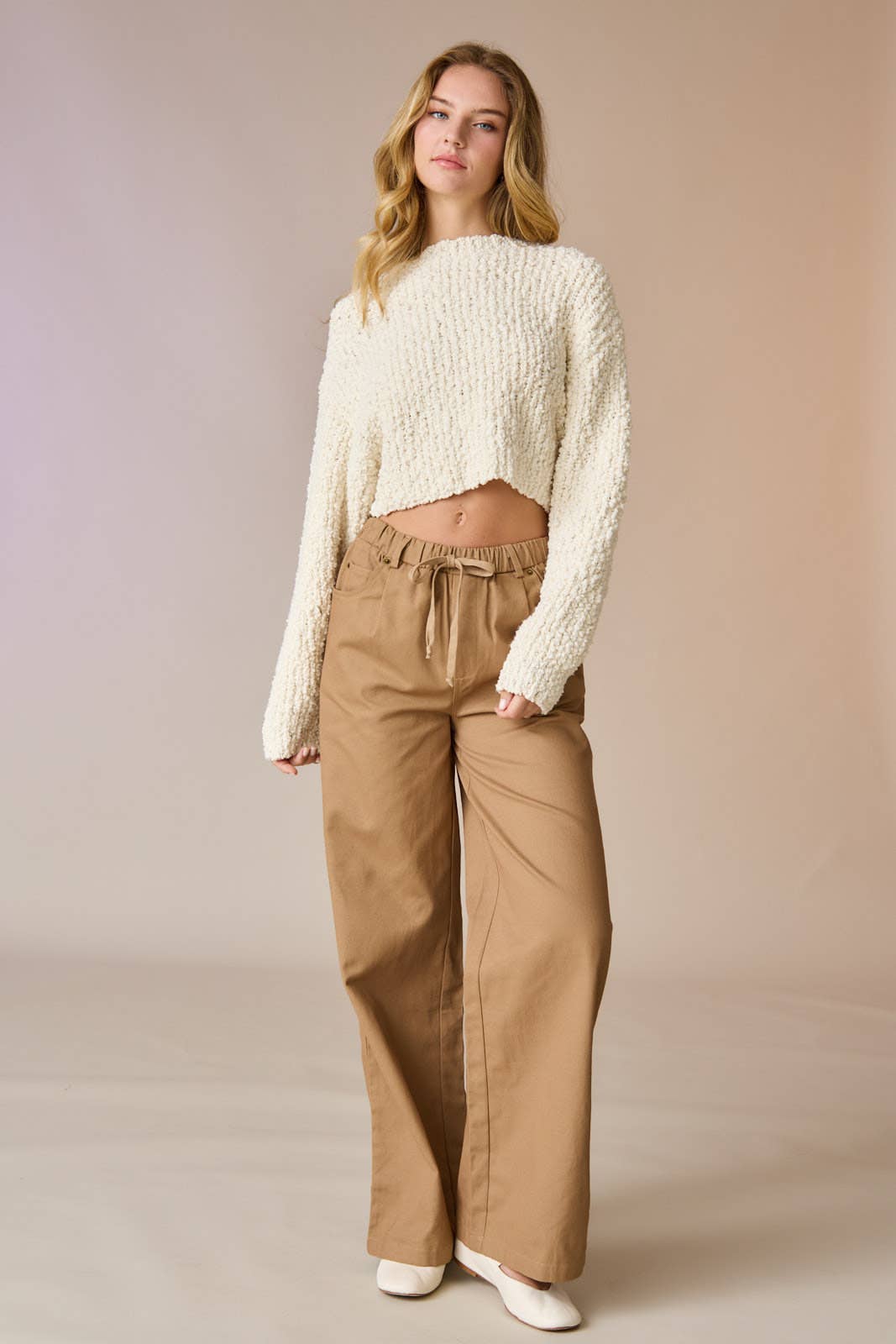 Woman wearing a cream popcorn knit cropped sweater with tan drawstring pants, hands in pockets.
