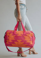 Bright orange and magenta woven weekender bag with geometric pattern, held by a woman in jeans