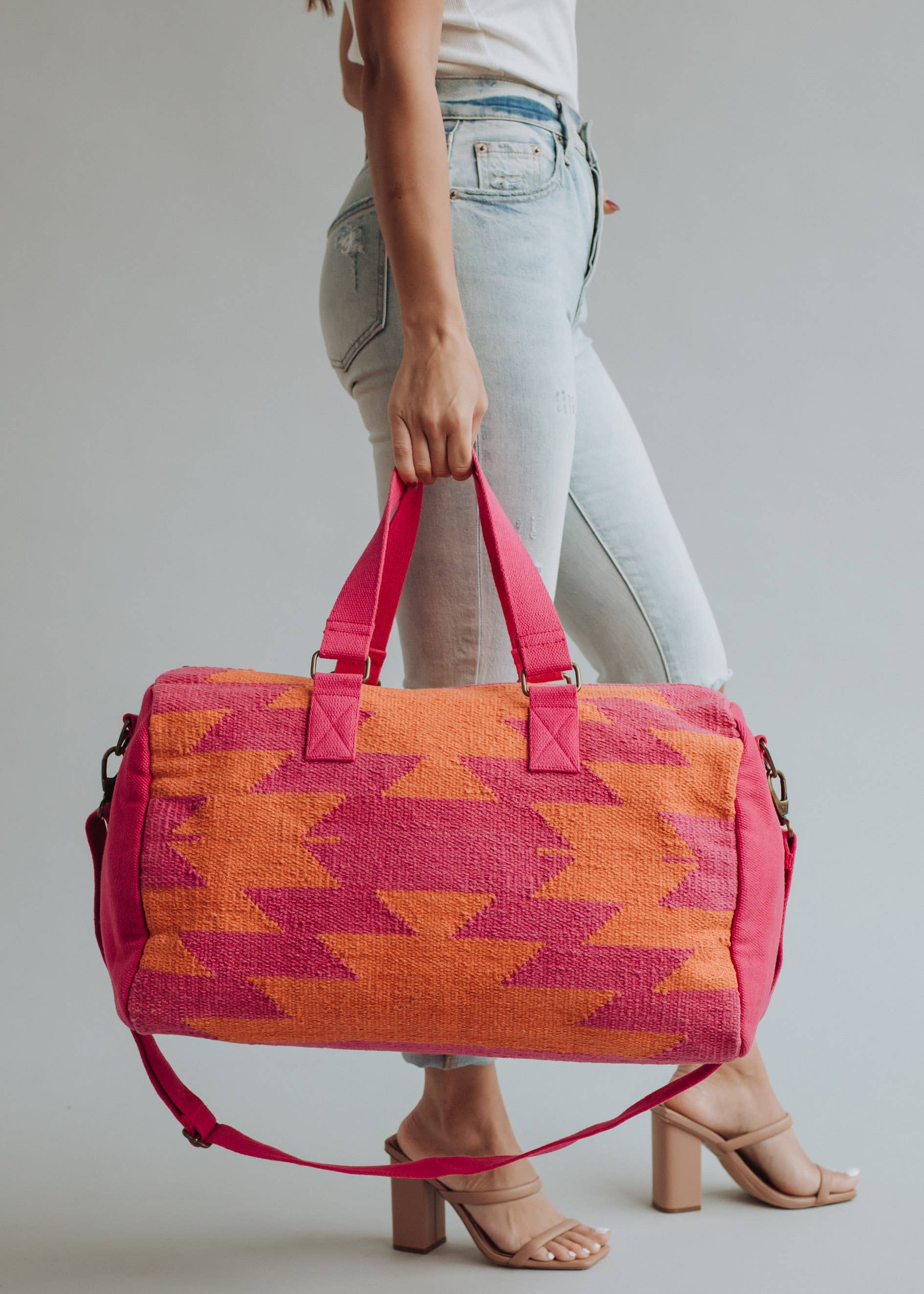 Bright orange and magenta woven weekender bag with geometric pattern, held by a woman in jeans