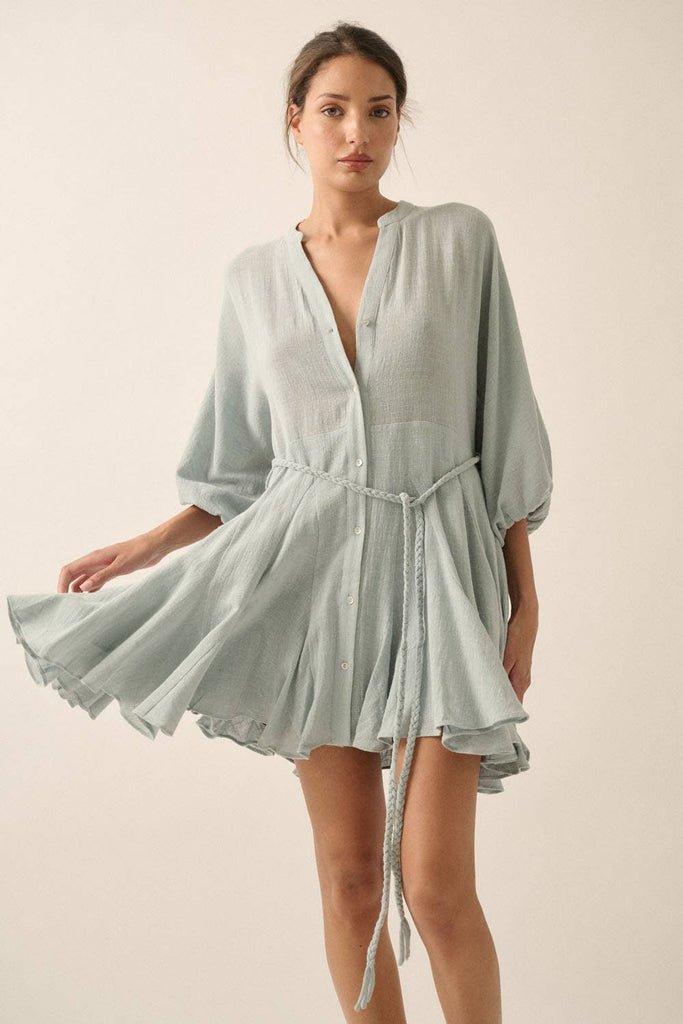 Woman wearing a sage green button-down mini dress with a braided waist tie and flowy hemline.