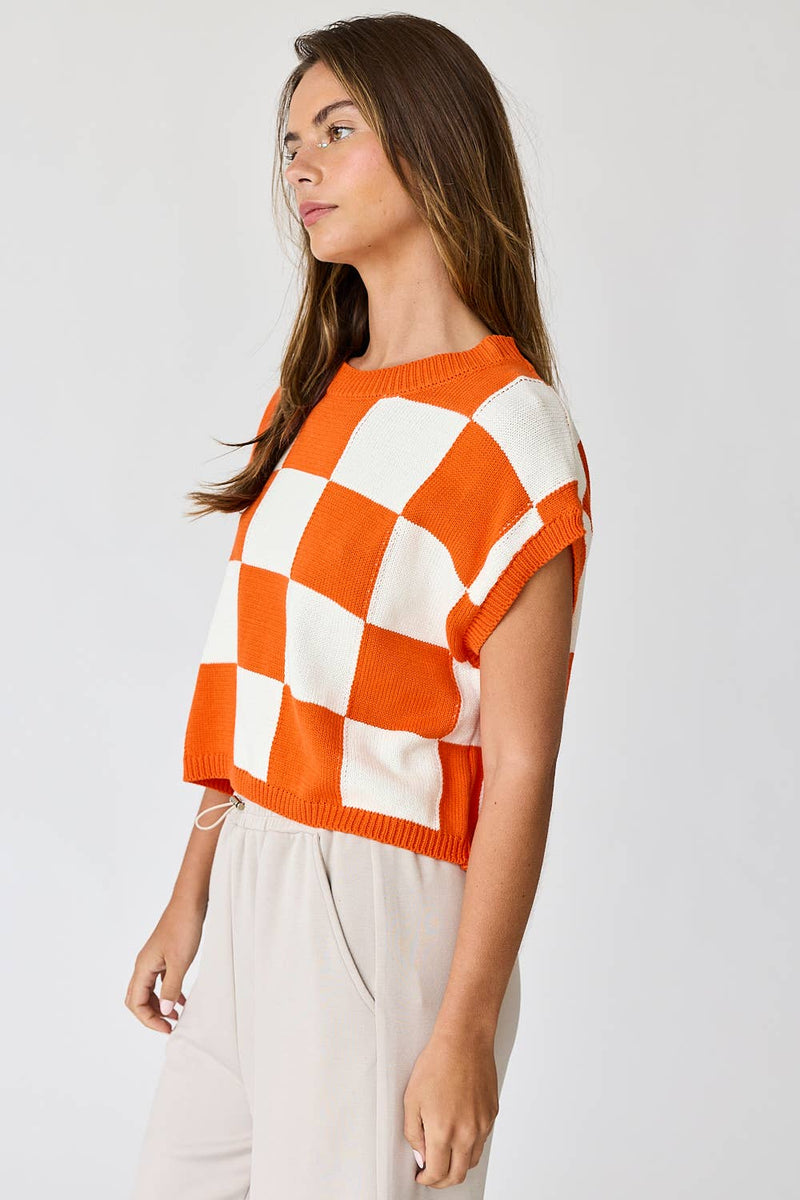 Woman wearing an orange and white loose-fit checker knit top with beige pants.