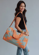 Wool woven orange and sage green weekender bag with geometric pattern, held by woman in jeans and black top