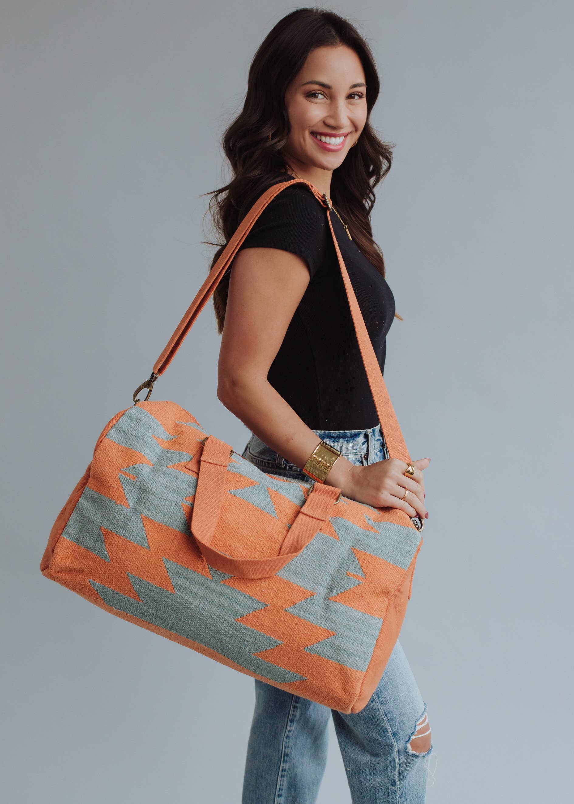 Wool woven orange and sage green weekender bag with geometric pattern, held by woman in jeans and black top