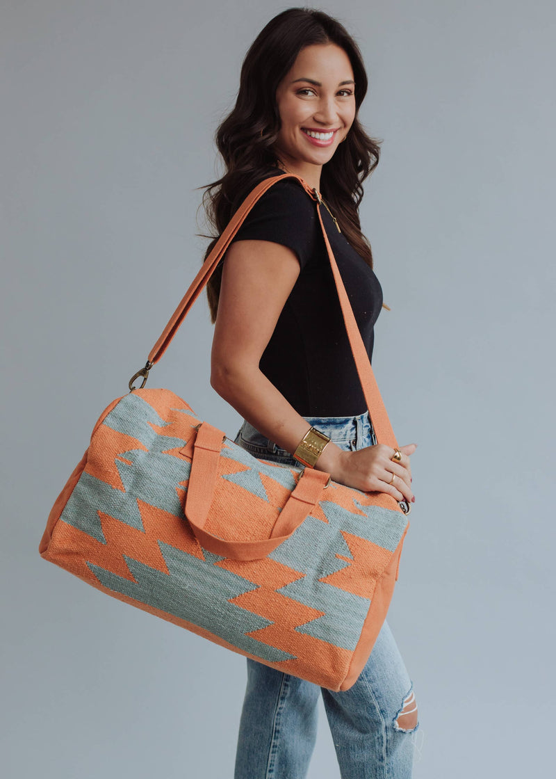 Wool woven orange and sage green weekender bag with geometric pattern, held by woman in jeans and black top